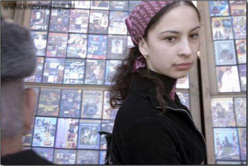 A young woman stands in front of a CD and DVD stand in Gr...